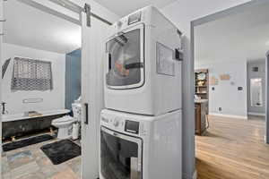 Laundry room featuring stacked washer / drying machine, a barn door, and light hardwood / wood-style flooring