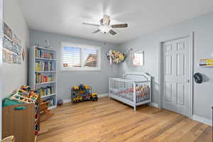 Bedroom featuring a crib, ceiling fan, and light wood-type flooring