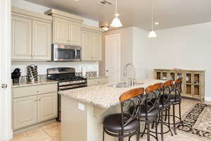 Kitchen with an island with sink, stainless steel appliances, decorative light fixtures, cream cabinets, and sink