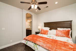 Bedroom with ensuite bathroom, ceiling fan, and dark carpet