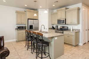 Kitchen featuring stainless steel appliances, sink, a kitchen island with sink, light stone counters, and cream cabinetry