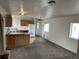 Kitchen with lofted ceiling, white refrigerator, a textured ceiling, light carpet, and kitchen peninsula