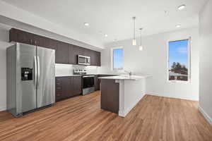 Kitchen with dark brown cabinets, light countertops, light wood-style flooring, a peninsula, and stainless steel appliances