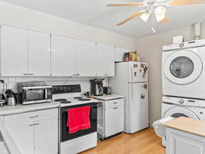 Kitchen with white appliances, stacked washer / dryer, light hardwood / wood-style floors, white cabinets, and decorative backsplash