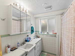 Bathroom with vanity, a textured ceiling, and tile walls