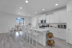 Kitchen featuring white cabinetry, a kitchen breakfast bar, an island with sink, and appliances with stainless steel finishes