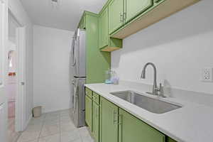 Laundry room with green cabinetry, stacked washing maching and dryer, sink, and light tile patterned floors