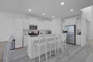 Kitchen featuring a breakfast bar, a kitchen island with sink, stainless steel appliances, white cabinets, and light wood-type flooring