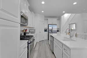 Kitchen with sink, appliances with stainless steel finishes, light hardwood / wood-style floors, white cabinets, and a center island with sink