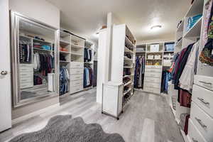 His and hers walk -in closet with light hardwood / wood-style floors and custom built-ins