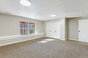 Unfurnished bedroom featuring baseboards, carpet flooring, a textured ceiling, and visible vents