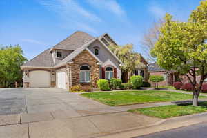 View of front of property featuring driveway, stone siding, an attached garage, a front yard, and stucco siding