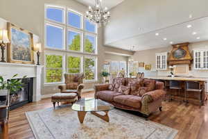 Living room featuring wood finished floors, an inviting chandelier, a towering ceiling, baseboards, and recessed lighting