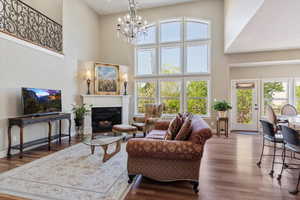 Living area with a towering ceiling, wood finished floors, baseboards, a glass covered fireplace, and a notable chandelier