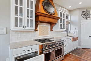 Kitchen with white cabinets, light stone counters, backsplash, wood finished floors, and range with two ovens