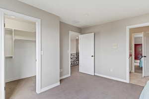 Unfurnished bedroom with light carpet, baseboards, a closet, and a walk in closet