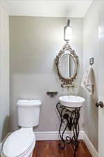 Half bathroom with wood finished floors, toilet, baseboards, and a sink