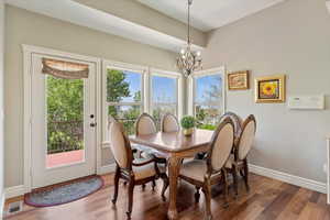 Dining space with baseboards, wood finished floors, visible vents, and a chandelier