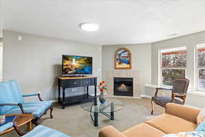 Carpeted living room featuring a textured ceiling, a tiled fireplace, visible vents, and baseboards
