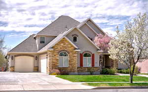 Craftsman-style house featuring driveway, stone siding, an attached garage, stucco siding, and roof with shingles