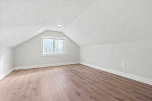 Bonus room featuring lofted ceiling, a textured ceiling, and light wood-type flooring