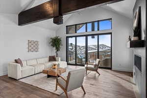 Living room featuring hardwood flooring, beam ceiling, a fireplace, high vaulted ceiling and views from deck.