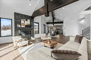 Living room featuring hardwood flooring, beam ceiling, a fireplace, high vaulted ceiling and views from side windows.