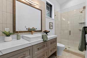 Main Level bathroom featuring walk in shower, toilet, tile walls, custom framed mirror, vanity, and tile patterned flooring