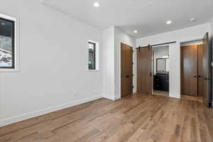 Unfurnished bedroom featuring connected bathroom, a barn door, and light hardwood / wood-style floors