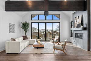 Living room featuring hardwood flooring, beam ceiling, a fireplace, high vaulted ceiling and views from deck.