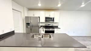 Kitchen featuring stainless steel appliances, sink, white cabinets, and light hardwood / wood-style floors