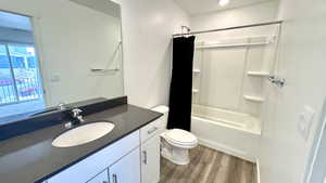 Full bathroom featuring hardwood / wood-style flooring, vanity, shower / bath combination with curtain, and toilet