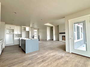 Kitchen featuring white cabinetry, a kitchen island with sink, a textured ceiling, and light wood-type flooring