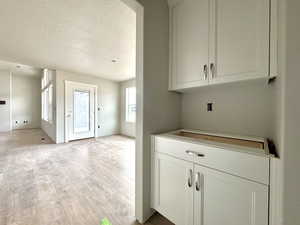 Kitchen featuring a textured ceiling, light hardwood / wood-style flooring, and white cabinets