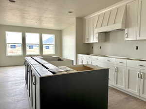 Kitchen with white cabinetry, a kitchen island, stovetop, and light hardwood / wood-style flooring