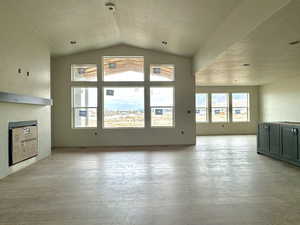 Unfurnished living room with light hardwood / wood-style flooring, a textured ceiling, and vaulted ceiling