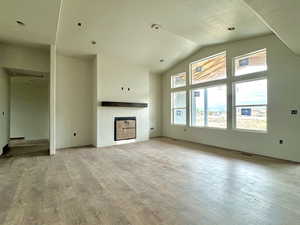 Unfurnished living room with lofted ceiling, a textured ceiling, and light wood-type flooring