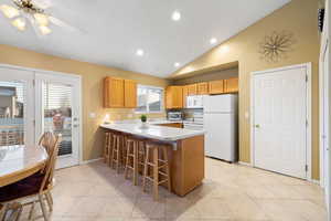 Kitchen featuring light tile patterned floors, white appliances, a breakfast bar area, vaulted ceiling, and kitchen peninsula