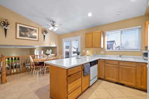 Kitchen with vaulted ceiling, light tile patterned flooring, sink, white dishwasher, and kitchen peninsula