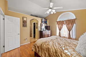 Bedroom featuring lofted ceiling, a walk in closet, ceiling fan, light hardwood / wood-style floors, and a closet