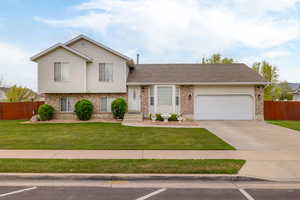 Split level home with brick siding, a front lawn, and fence