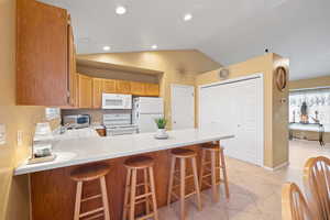 Kitchen featuring a kitchen breakfast bar, sink, white appliances, and kitchen peninsula