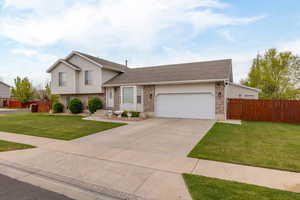 Tri-level home featuring roof with shingles, fence, brick siding, a garage, and a front yard