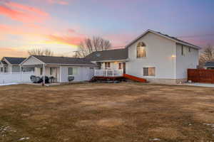 Back house at dusk with a wooden deck, a yard, and a patio area