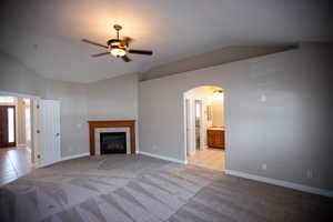 Master Suite featuring ceiling fan, a tiled fireplace, vaulted ceiling, and light carpet