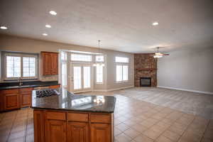 Kitchen featuring light tile patterned flooring, a stone fireplace, decorative light fixtures, sink, and dark granite counters