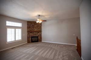 Great room with ceiling fan, a stone fireplace, carpet floors, and a textured ceiling