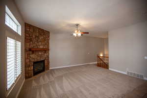 Great room featuring a stone fireplace, carpet floors, a textured ceiling, and ceiling fan