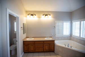 Master Suite bath with a relaxing tiled tub, vanity, toilet, jetted tub and tile patterned flooring