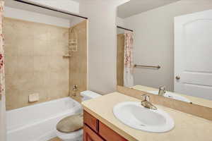 Full bathroom with vanity, shower / bathtub combination with curtain, and toilet